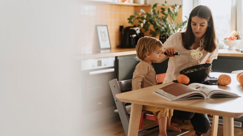 A mom and her child baking in a cozy kitchen surrounded by pumpkins.